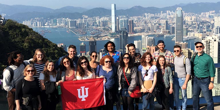 A group of students hold an IU flag during a trip with the Hong Kong cityscape in the background.