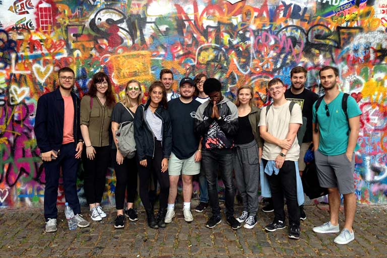 A group of students stands in front of a wall covered in graffiti.