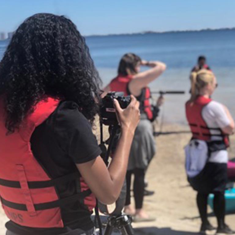 A group of students use audiovisual equipment on a beach.