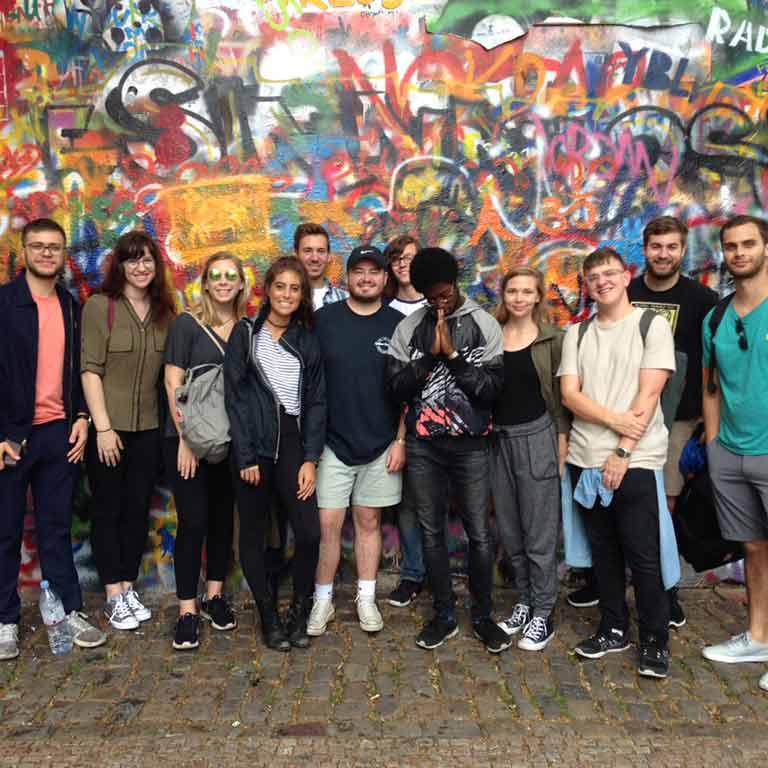 A group of students stand in front of a wall covered in graffiti.