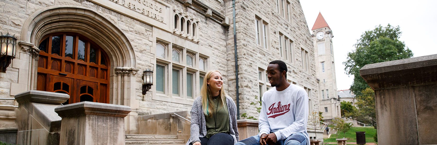 Two students sit and talk on the stairs at the Franklin Hall main entrance.
