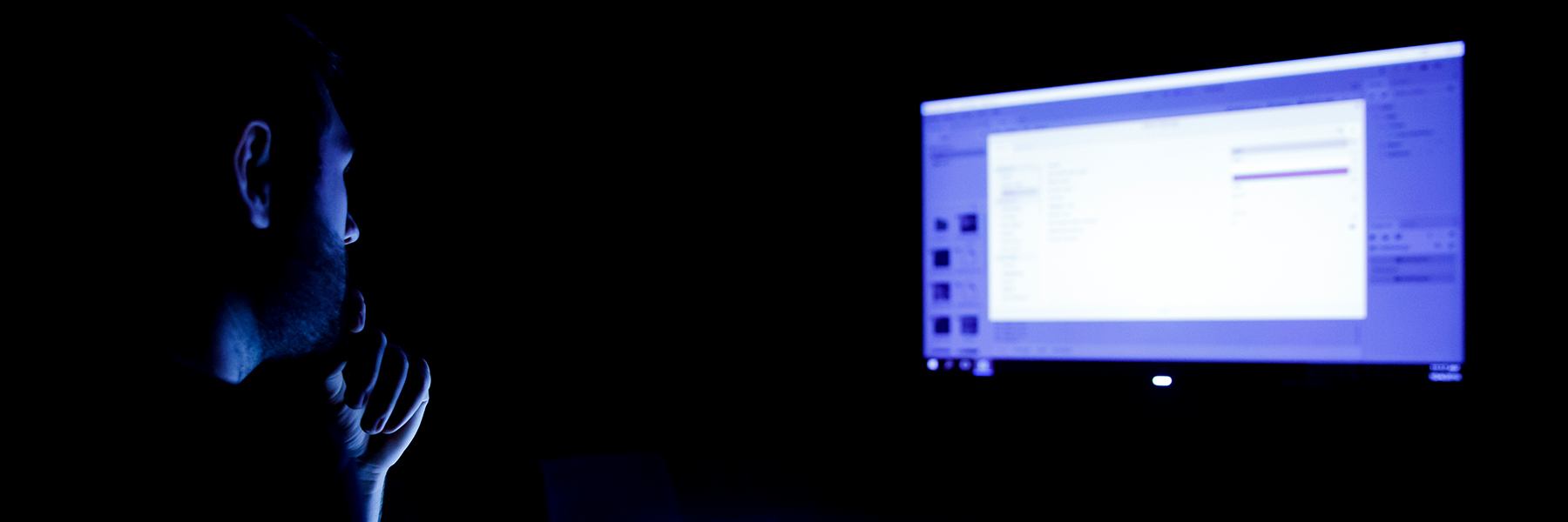A student looks at a monitor in a dark room while he works on a digital project.