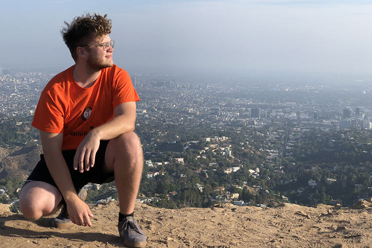 A student kneels on a rock ledge looking over the city of Los Angeles.