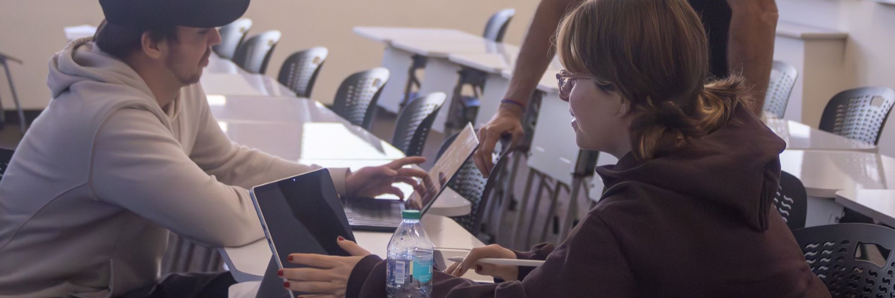 Two people seated in a classroom working on laptops.