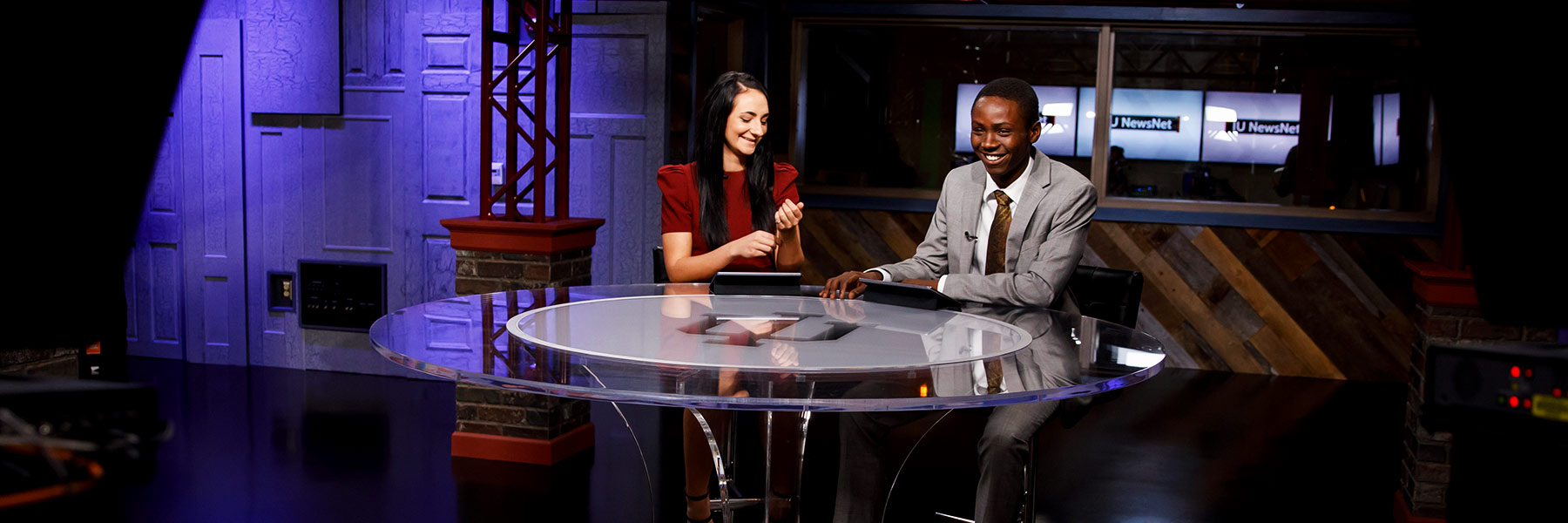 Two students sitting at a table in the TV studio prepare for a broadcast.