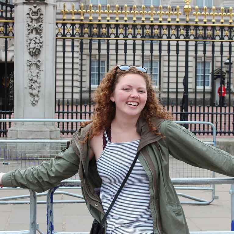 A student smiles and poses in front of the Buckingham Palace Gates during a trip in London. 