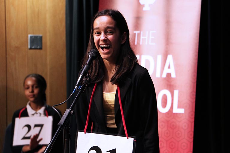 A girl at the stage microphone smiles during the Scripps Regional Spelling Bee.