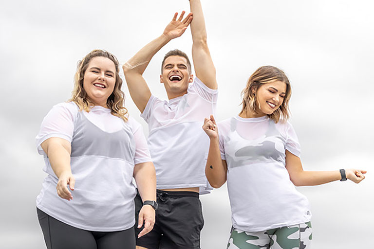Three people wearing white t-shirts dance outdoors.