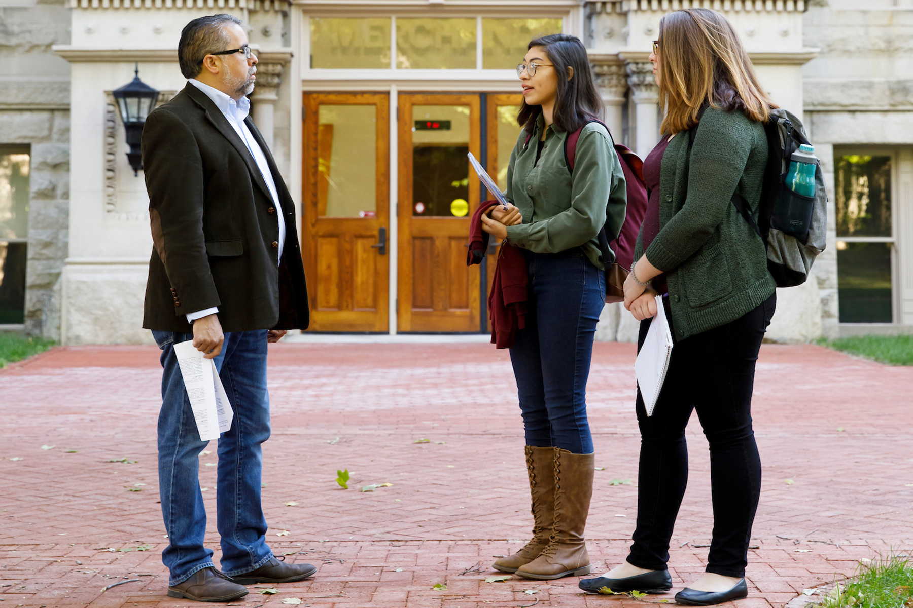 Two students speak with Prof. Gerry Lanosga outside on campus.