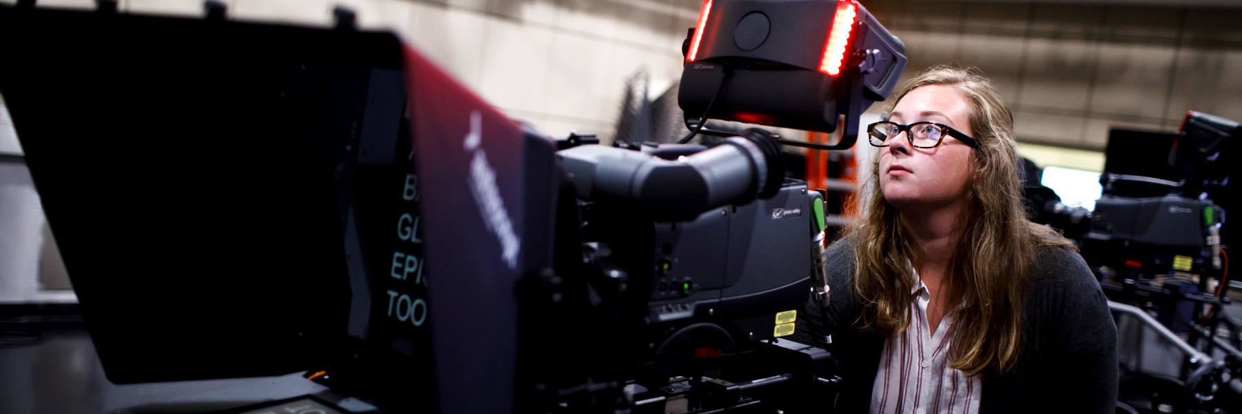 A student sits behind a TV camera.