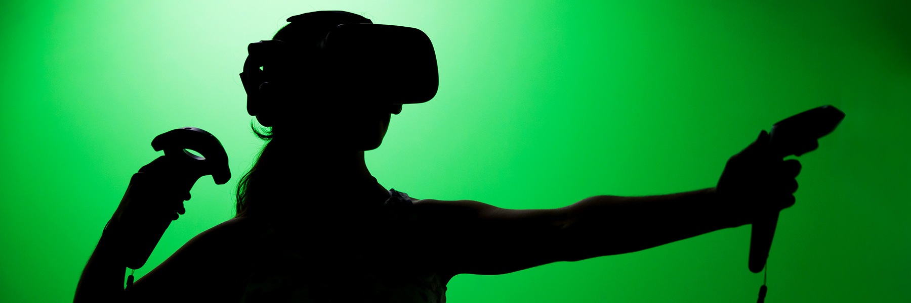 A silhouette of a person with a virtual reality headset and a controller in front of a green screen