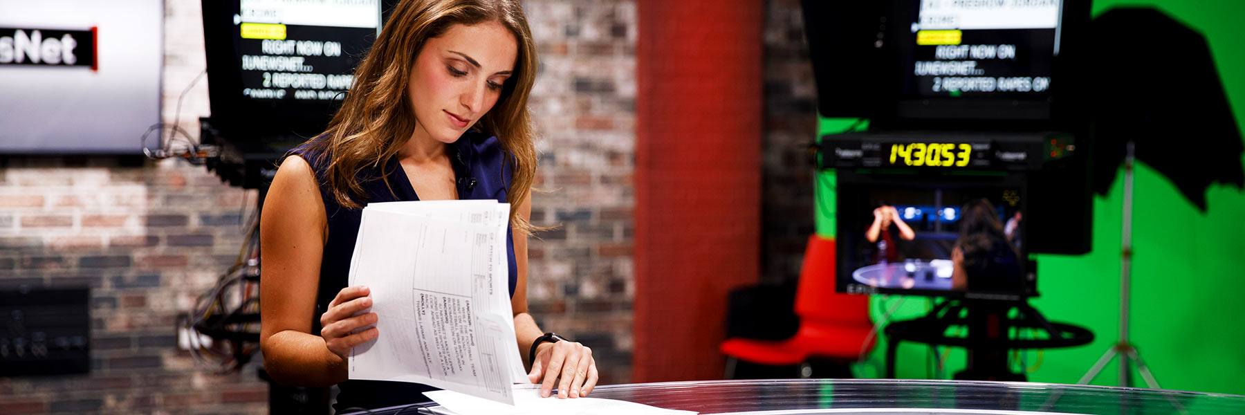 A student reporter looks at a script in a TV studio.