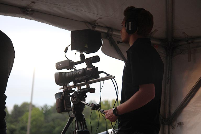 A student works with a video camera under a tent outside.