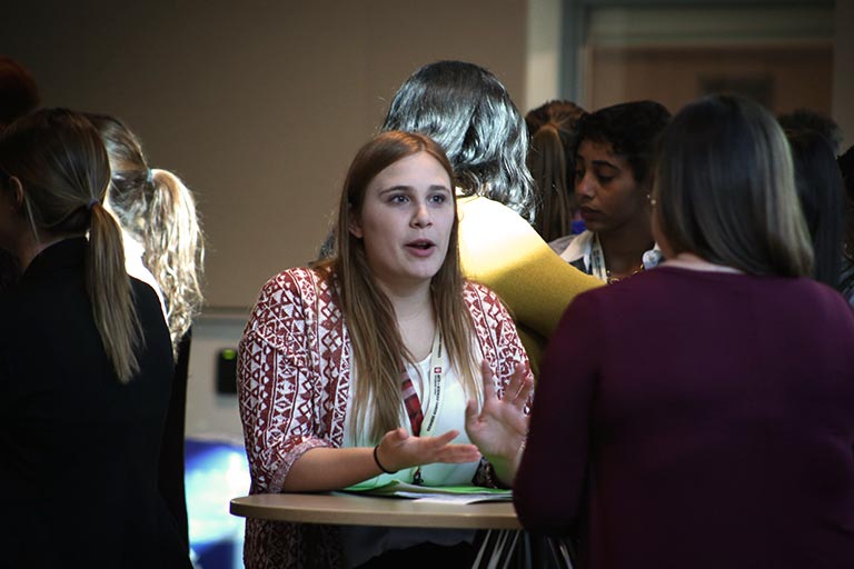 A student talks with a corporate representative at a table during a networking session.