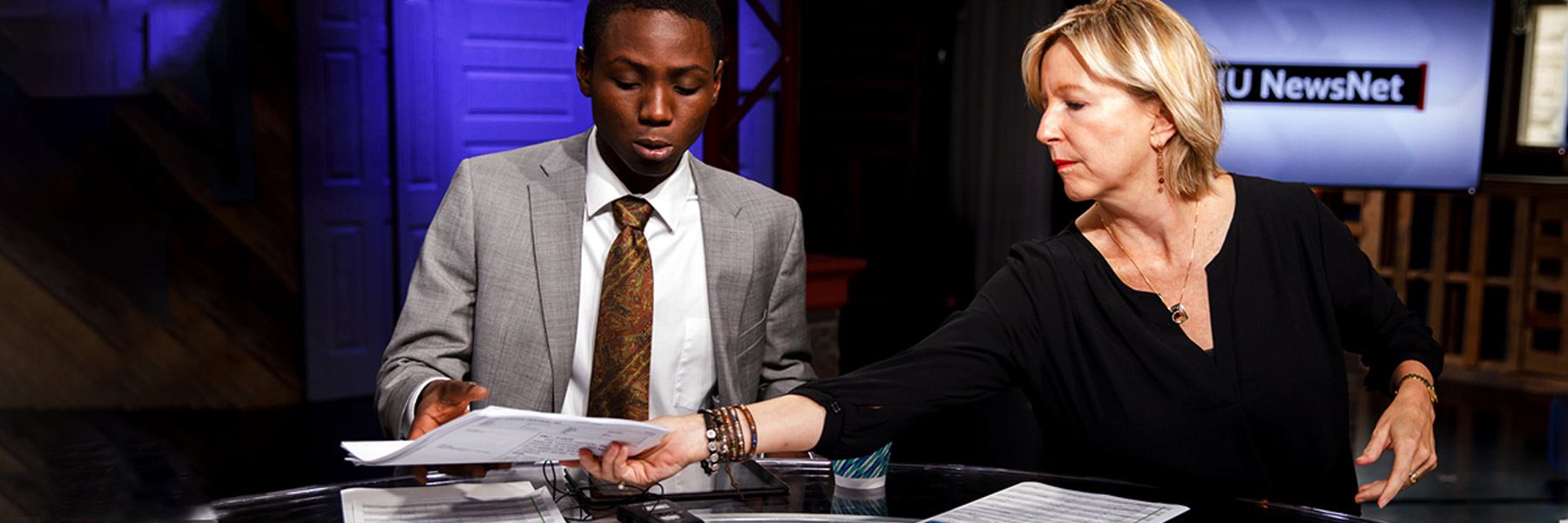 A student and a reporter sit at a table in a TV studio.