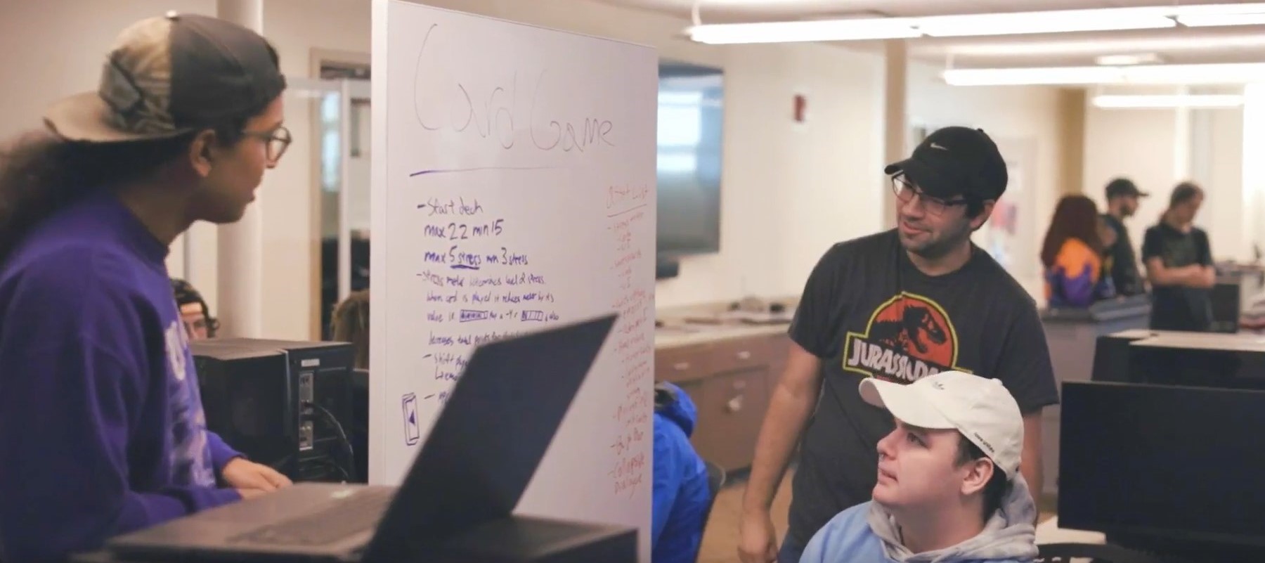 Three people stand near a whiteboard in mid-conversation.