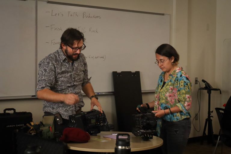 Two people in a classroom work on pieces of equipment laid out on a table.