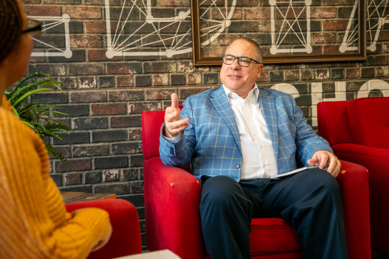 Kevin Corcoran sits in a chair and talks to an interviewer.