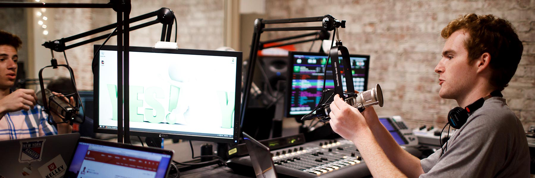 Two students operate the equipment in a radio studio.