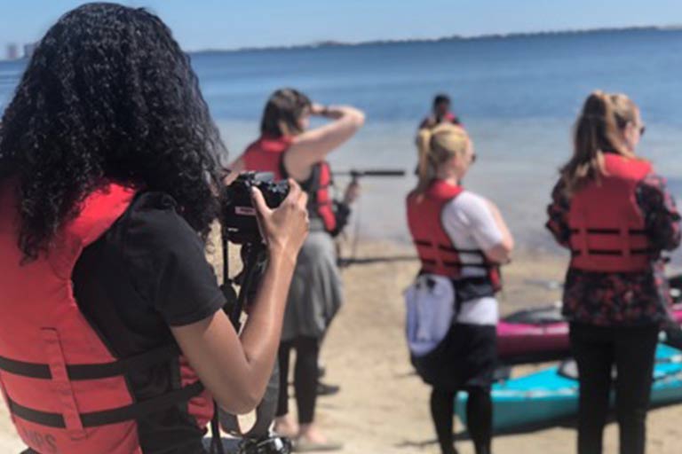 A group of students uses audiovisual equipment on a beach.