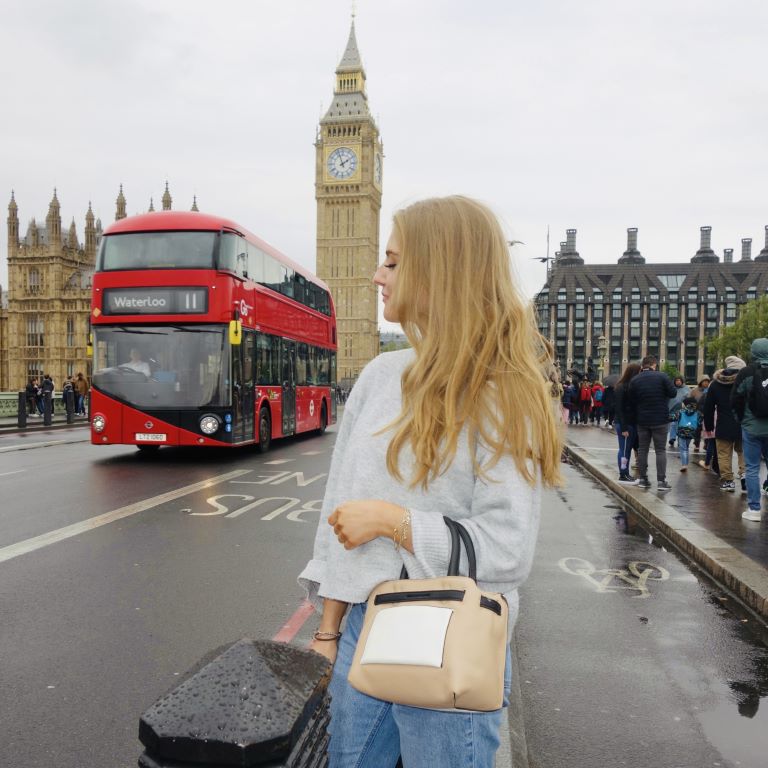 Person stands outside in London on an overcast day with the iconic Big Ben clock and red double-decker bus behind them.