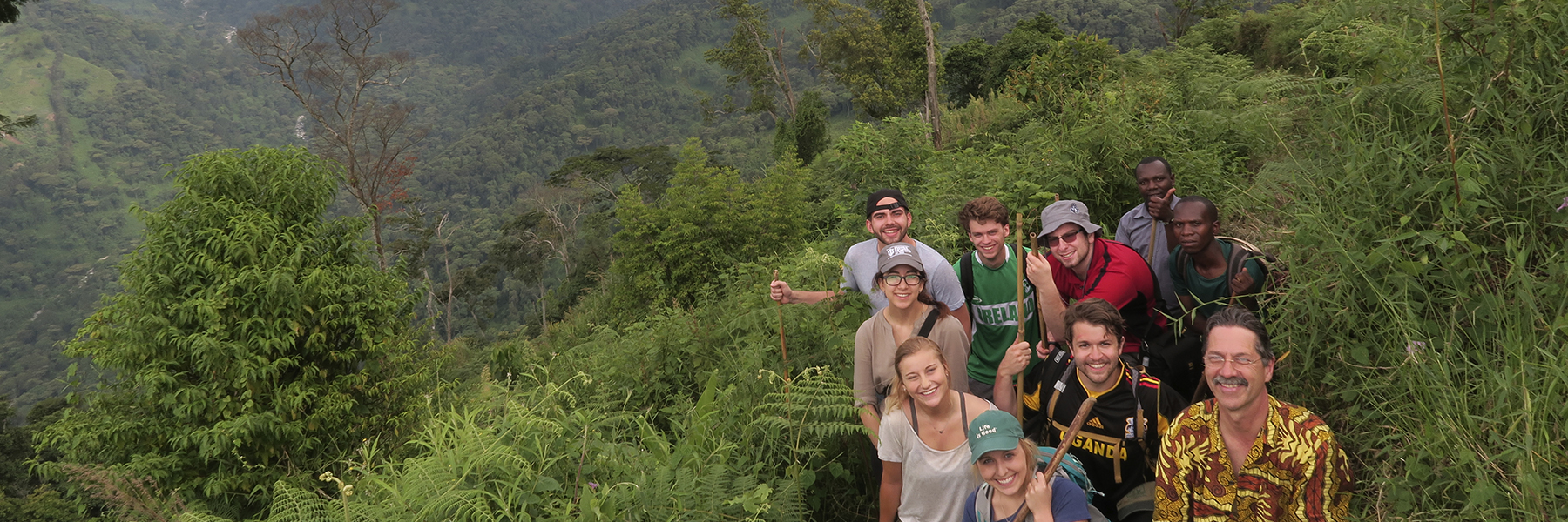 A group of students stands on a overgrown hillside above a valley.