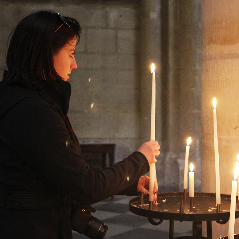 A woman adds a lit candle to a group of other lit candles on a round candleholder.