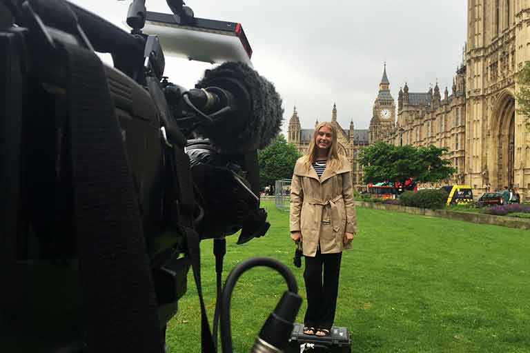 A woman standing in front of a camera in front of the Palace of Westminster